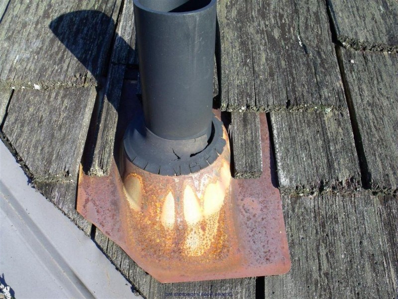 Rusted flashing around a boot pipe on a cedar shake roof. 