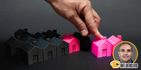 Image of a hand moving a pink house miniature. In the background are similar houses in black. John Kenney